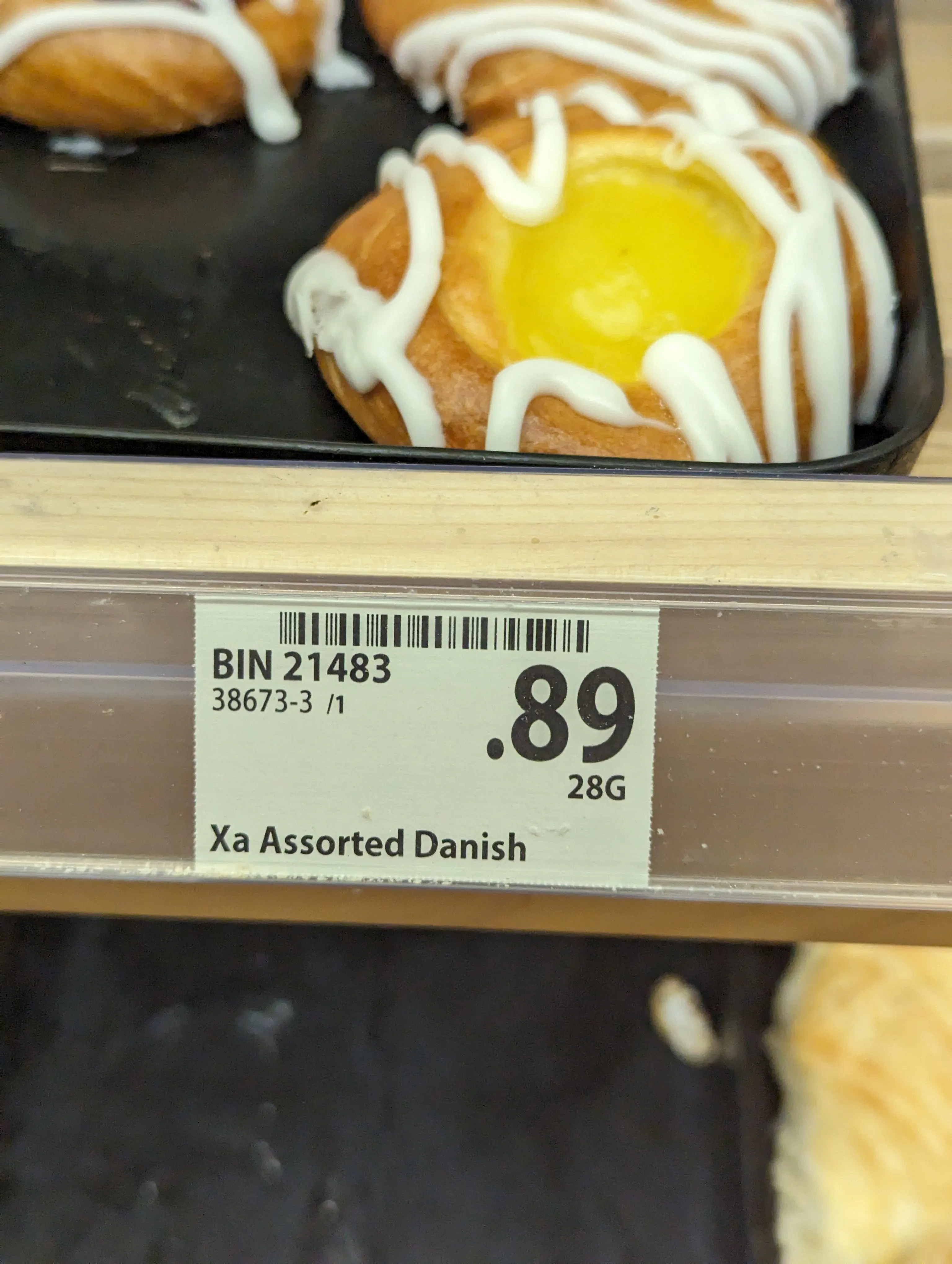 A danish in a bakery tray. you can clearly see the tag as well as some donuts below. The photo is blurry and not really in focus.
